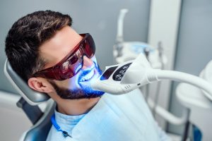 Smiling man receiving Teeth Whitening treatment with UV light.