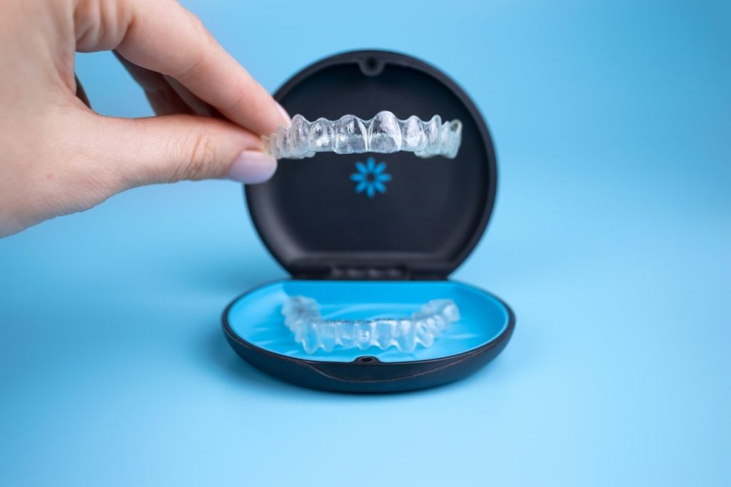 Female hand holding Invisalign retainers above its case.