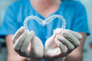 Female dentist holding two Invisalign transparent retainers in the shape of a heart.